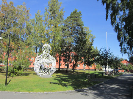 Bild från området på Umedalen där Västangårds fritidsgård ligger. Bland träd syns en stor skulptur som föreställer en hukande människofigur.