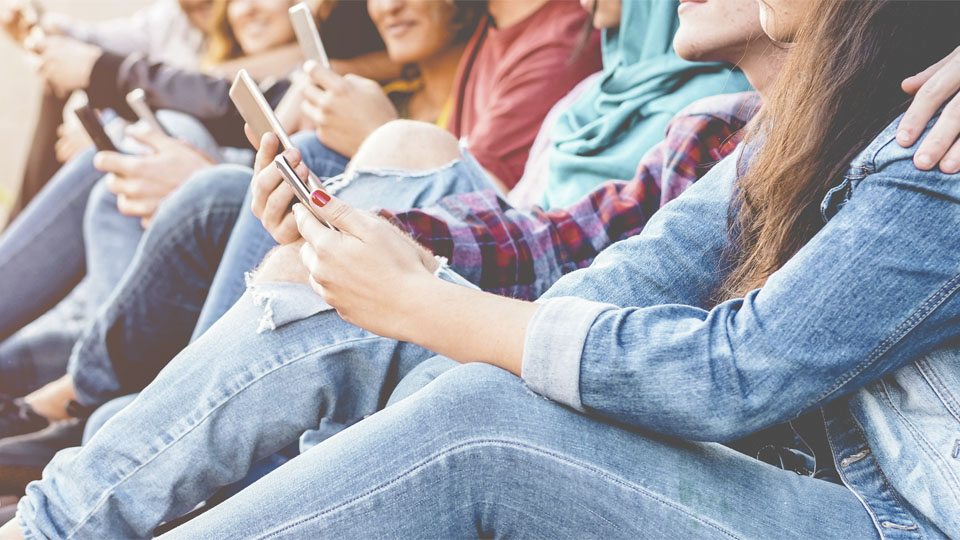 En grupp ungdomar sitter tillsammans och umgås. Några har mobiltelefoner i hand.